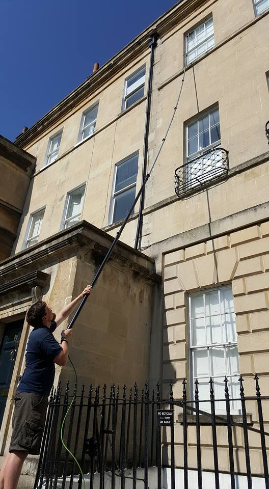 A window cleaner is cleaning a georgian house in Bath, UK. He is using a long reach pole to clean the top windows.